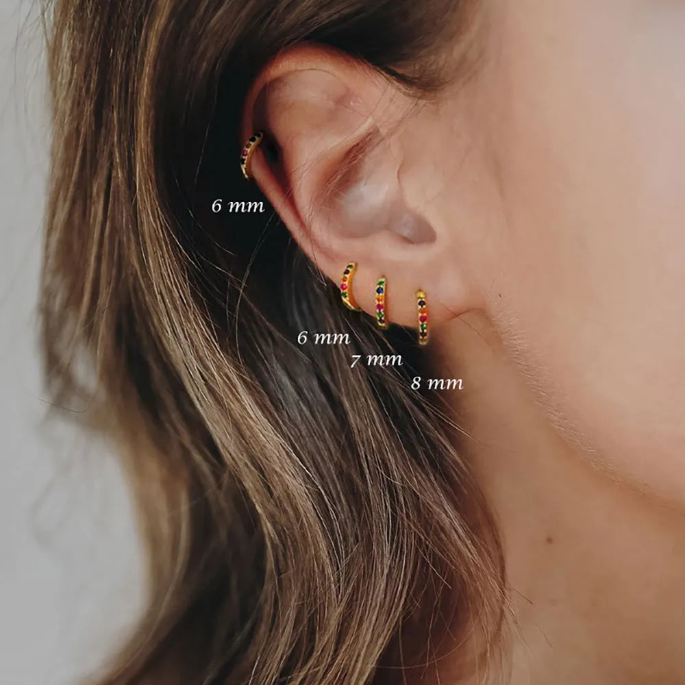 A pair of small circular zircon stud earrings with a metallic finish, shown next to a ruler indicating available sizes from 5mm to 12mm.