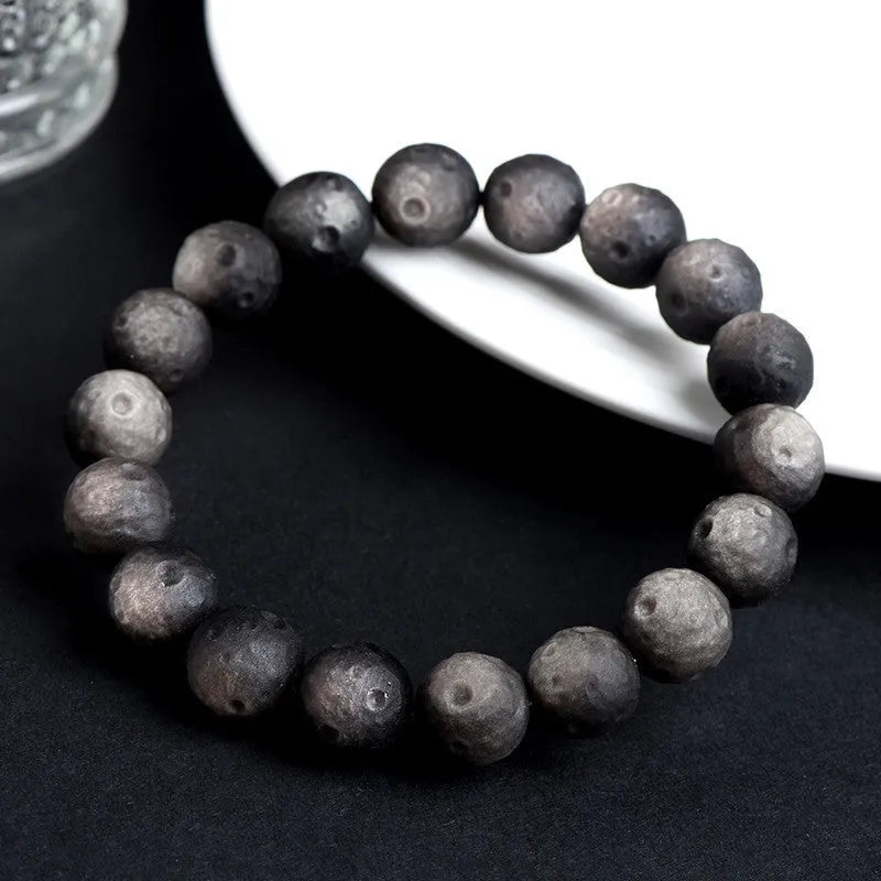 Close-up of an obsidian crater ball bead bracelet showing textured surface from grinding treatment, in silver stone meteorite finish.