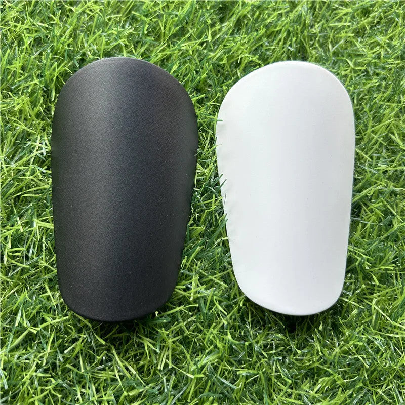 Extra small black and white plastic football shin guards for junior players, size 8cm by 5cm.