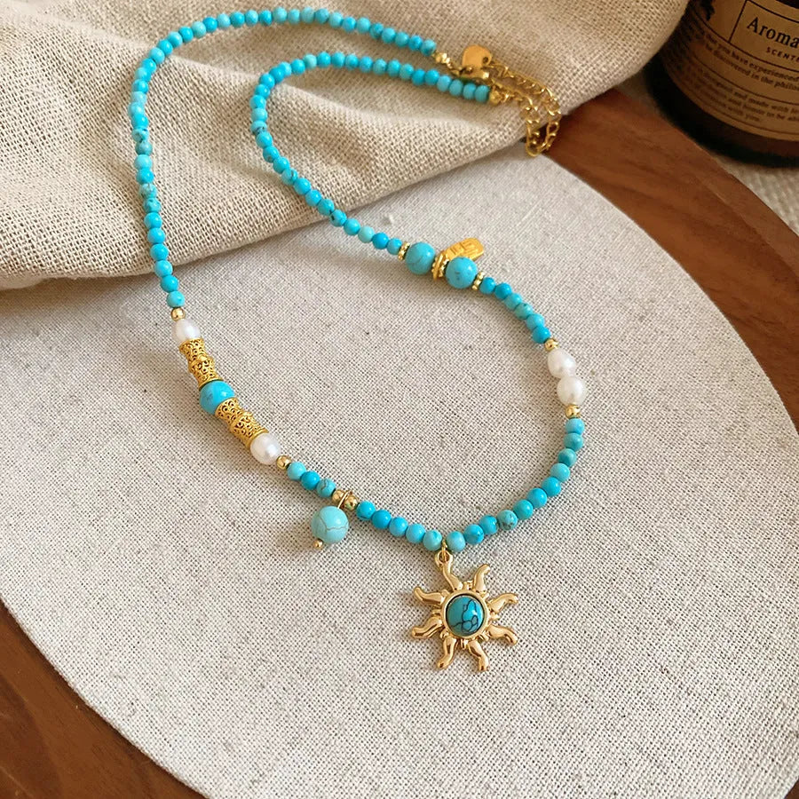 Freshwater pearl necklace with a geometric stone sun pendant on a gold, blue, and pink chain.