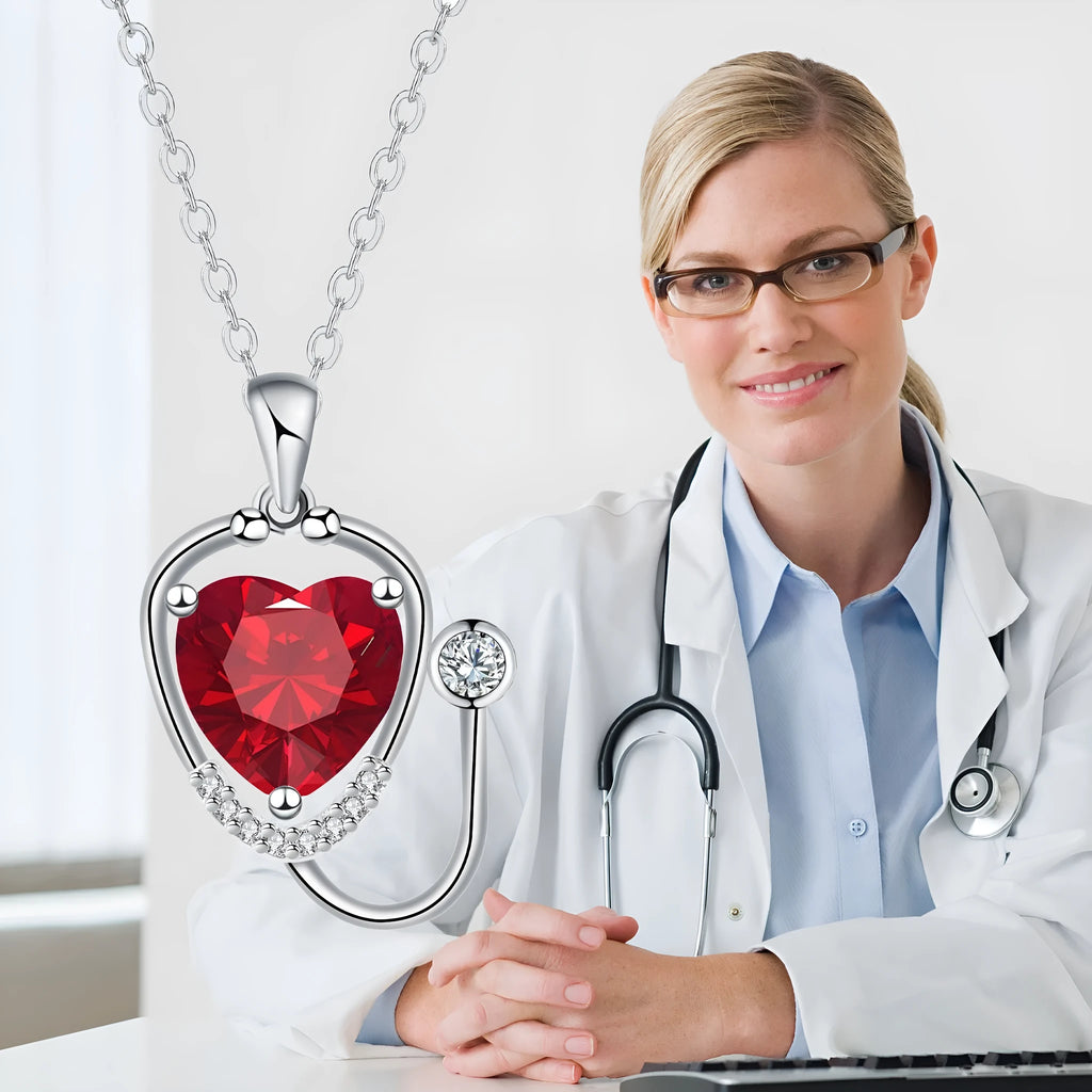 Close-up of a red diamond coloured stethoscope pendant necklace with cross, heart and wing details on a copper chain.