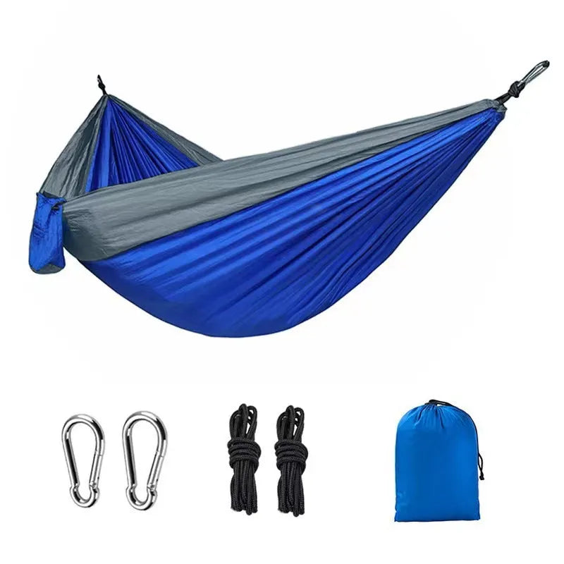 Blue nylon parachute cloth camping hammock hung between two trees outdoors.
