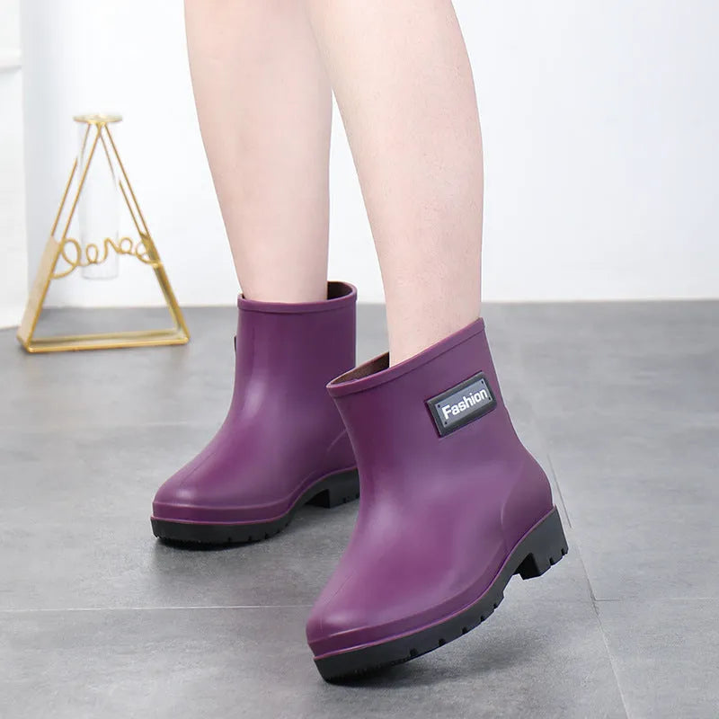 Women's black PVC mid-calf rain boot with low heel on a wet surface