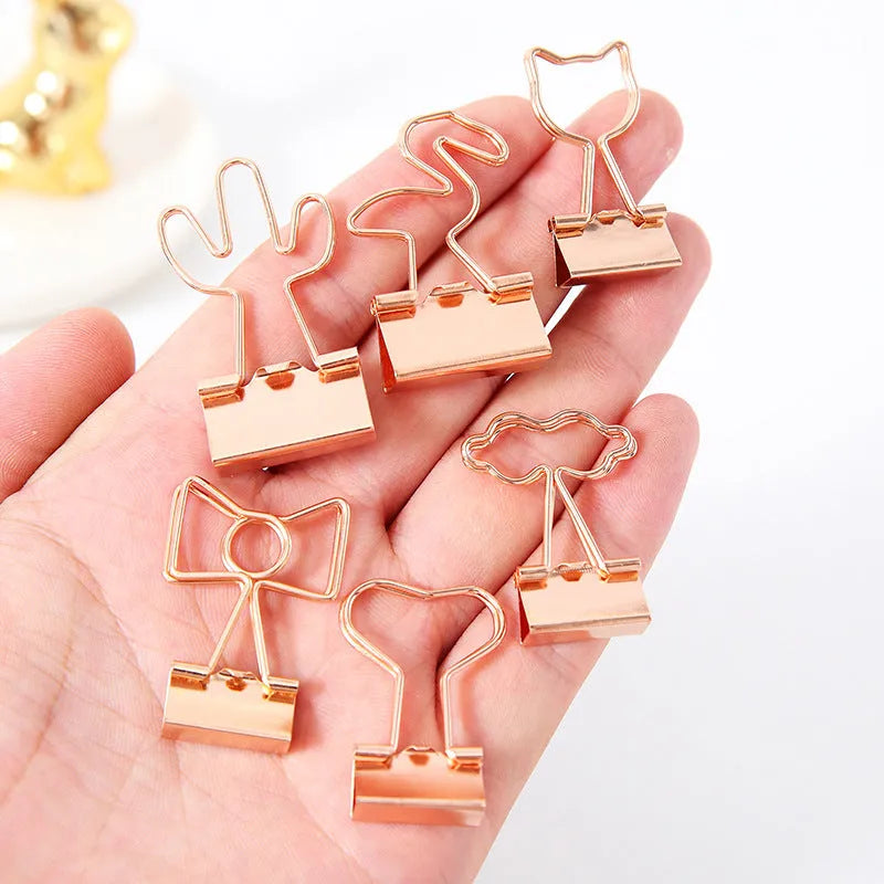 Gold-coloured decorative office paper clips with long tail designs including flamingo, love, cloud, cat, cactus, and bow shapes