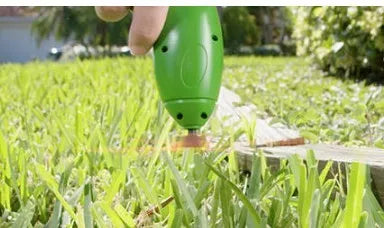 Cordless electric lawn trimmer with extension pole and black debris shield on a green lawn.