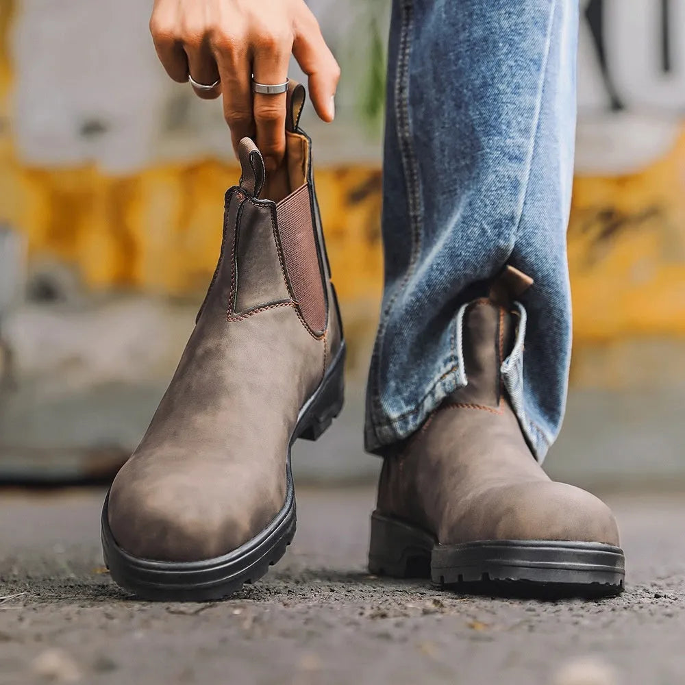 Vintage brown unisex Chelsea ankle boots with car suture stitching and a low heel on a wooden floor.