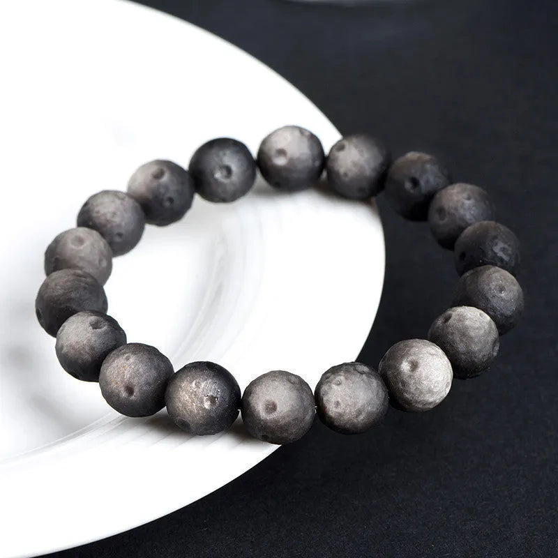 Close-up of an obsidian crater ball bead bracelet showing textured surface from grinding treatment, in silver stone meteorite finish.
