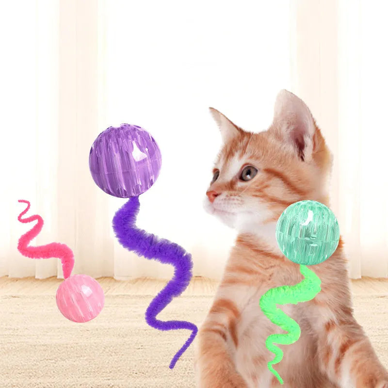 Green TPR bouncy cat toy with a long plush tail on a wooden floor.