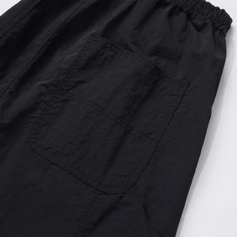 Black paratrooper trousers with elastic waist and drawstring closure, showing baggy fit and three-dimensional cutting