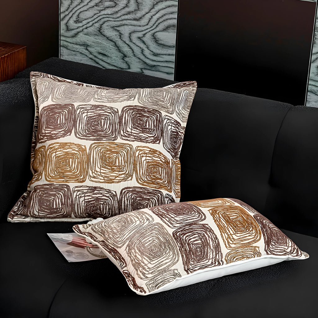 Square and rectangular pillow covers with cream and coffee abstract coil pattern on a sofa.