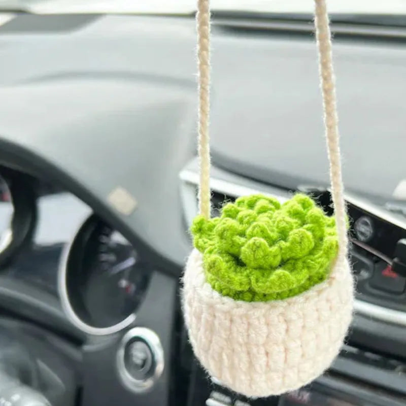 Green and white knitted car plant decoration with hanging rope on car dashboard