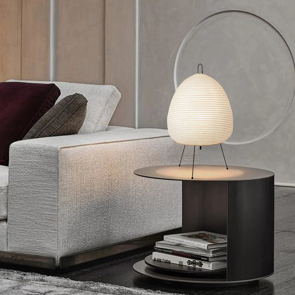 Japanese style table lamp with a white handmade paper lantern shade and aluminium base on a wooden table.