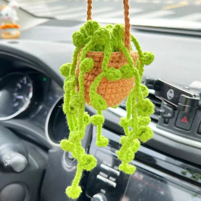 Green and white knitted car plant decoration with hanging rope on car dashboard