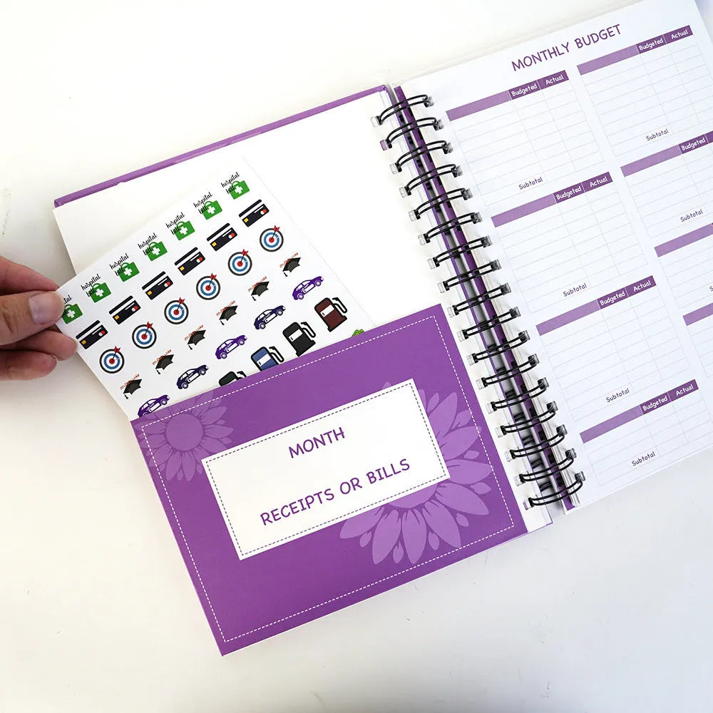 Purple coil-bound A5 financial planning notebook with pen, stickers, and paper clips for monthly budgeting