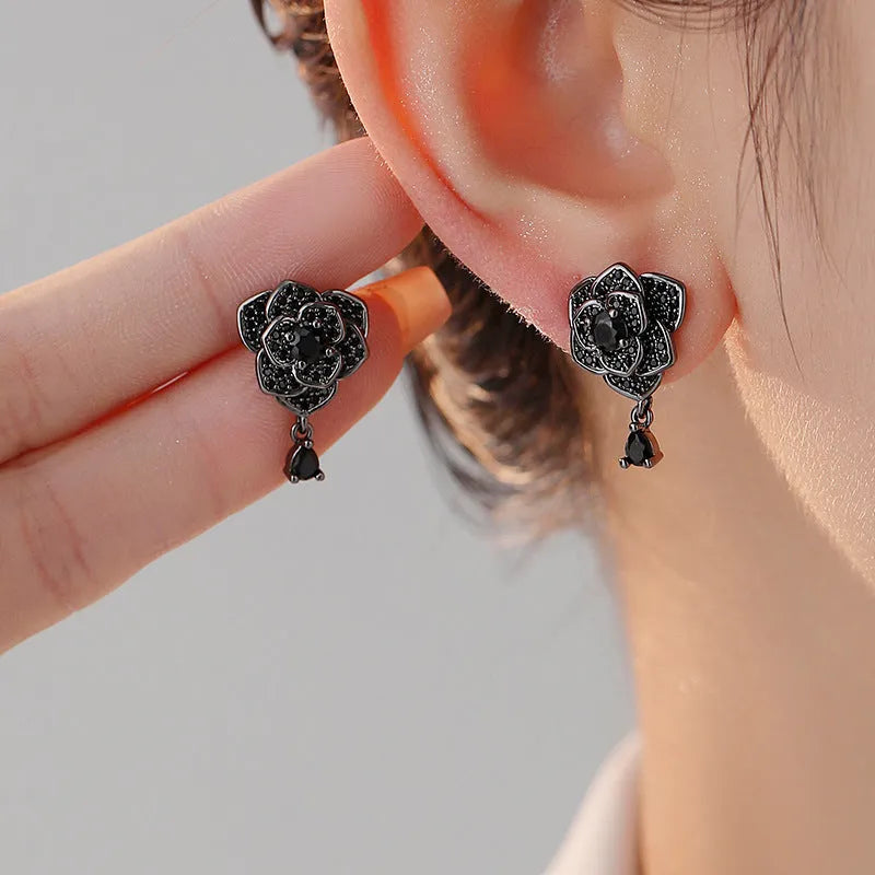Close-up of women's floral stud earrings with a black rose zircon stone and gold electroplated finish.