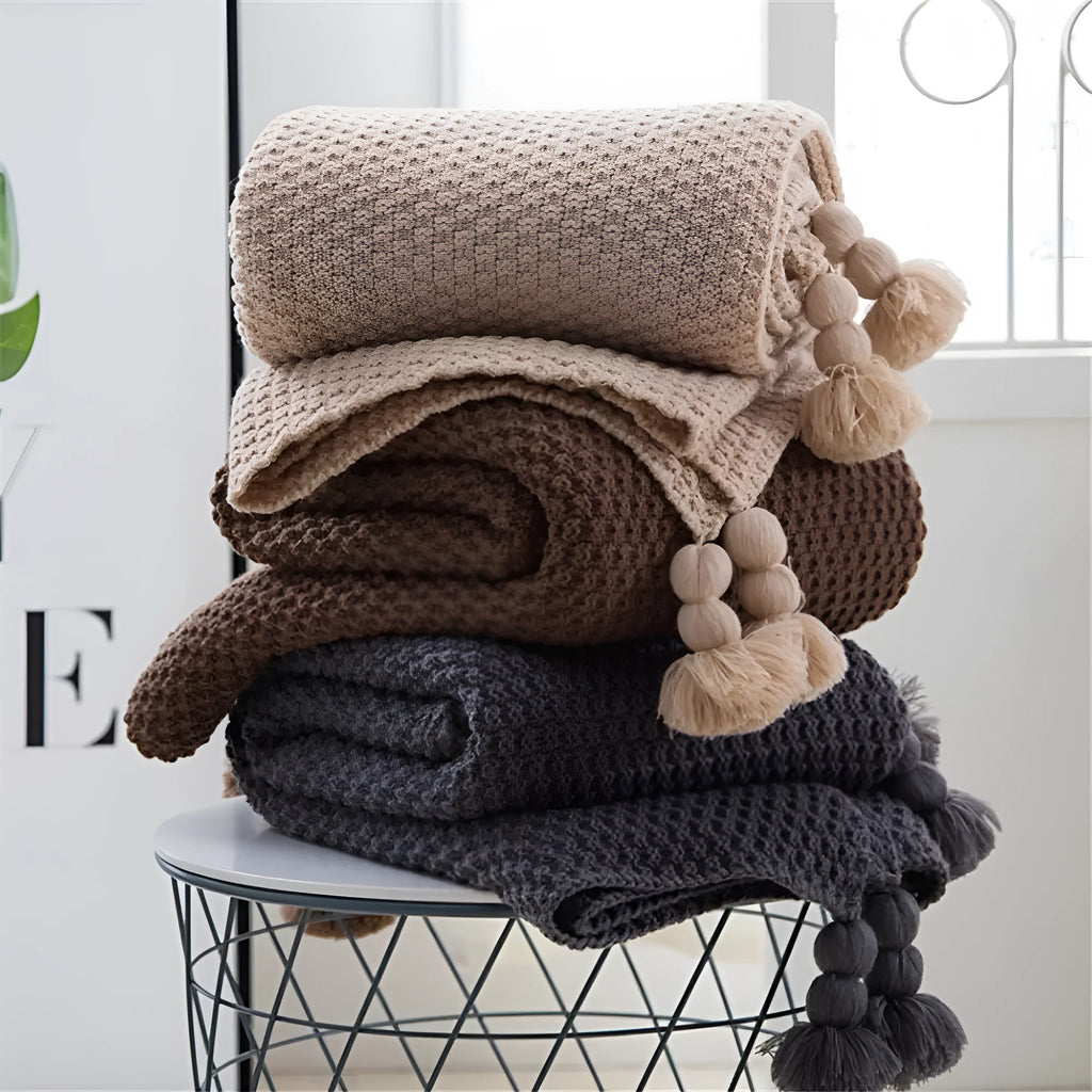 Nordic-style beige acrylic blanket with fringed knit ball detail laid flat.