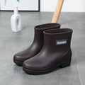 Women's black PVC mid-calf rain boot with low heel on a wet surface