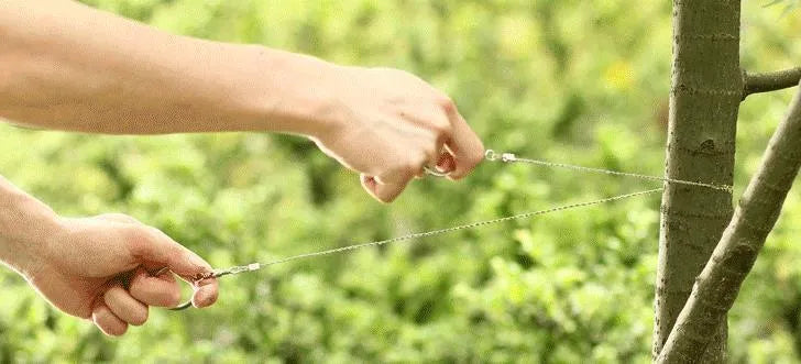 A coiled black or red survival wire saw made of braided stainless steel, shown with a scale indicating its small size.