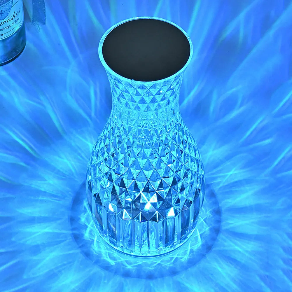White crystal vase-shaped table lamp with remote control on a wooden surface.