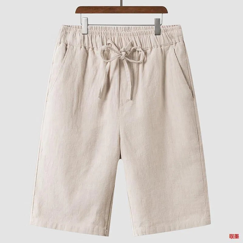 Men's beige linen shorts with loose cropped fit and elasticated waistband laid flat.