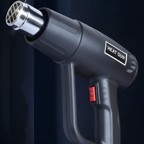 Black industrial hot air gun with a two-speed switch and grid-pattern nozzle on a workbench.