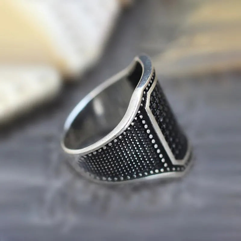Black alloy ring with copper inlay detail and set zircon stones, shown on a hand.