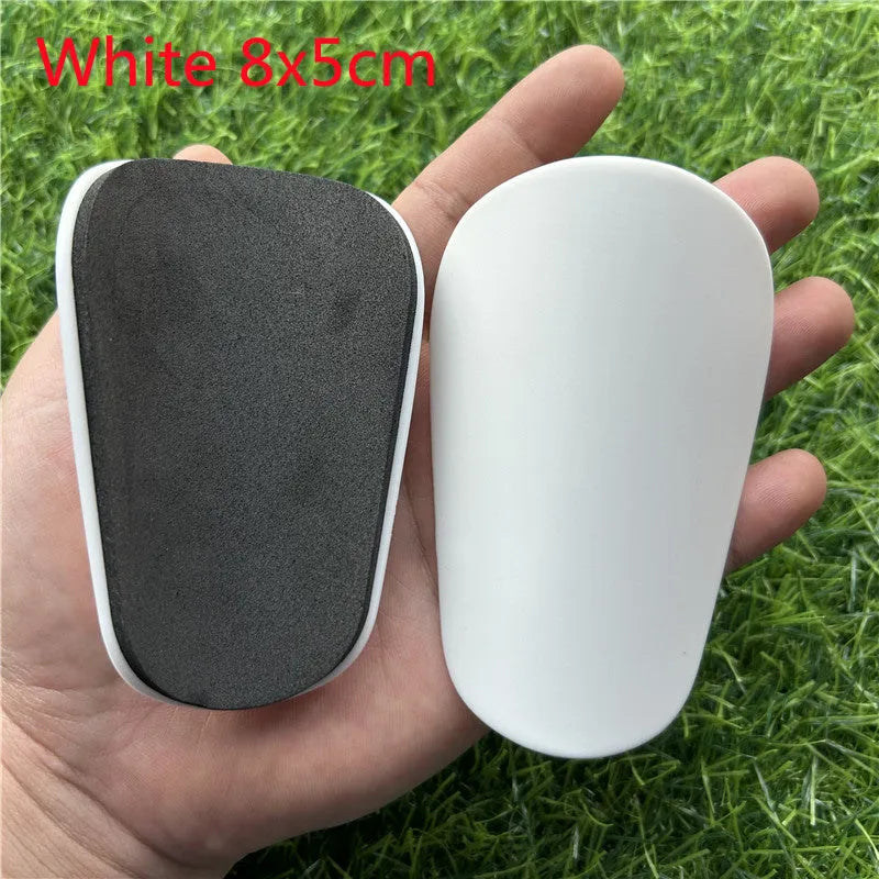 Extra small black and white plastic football shin guards for junior players, size 8cm by 5cm.