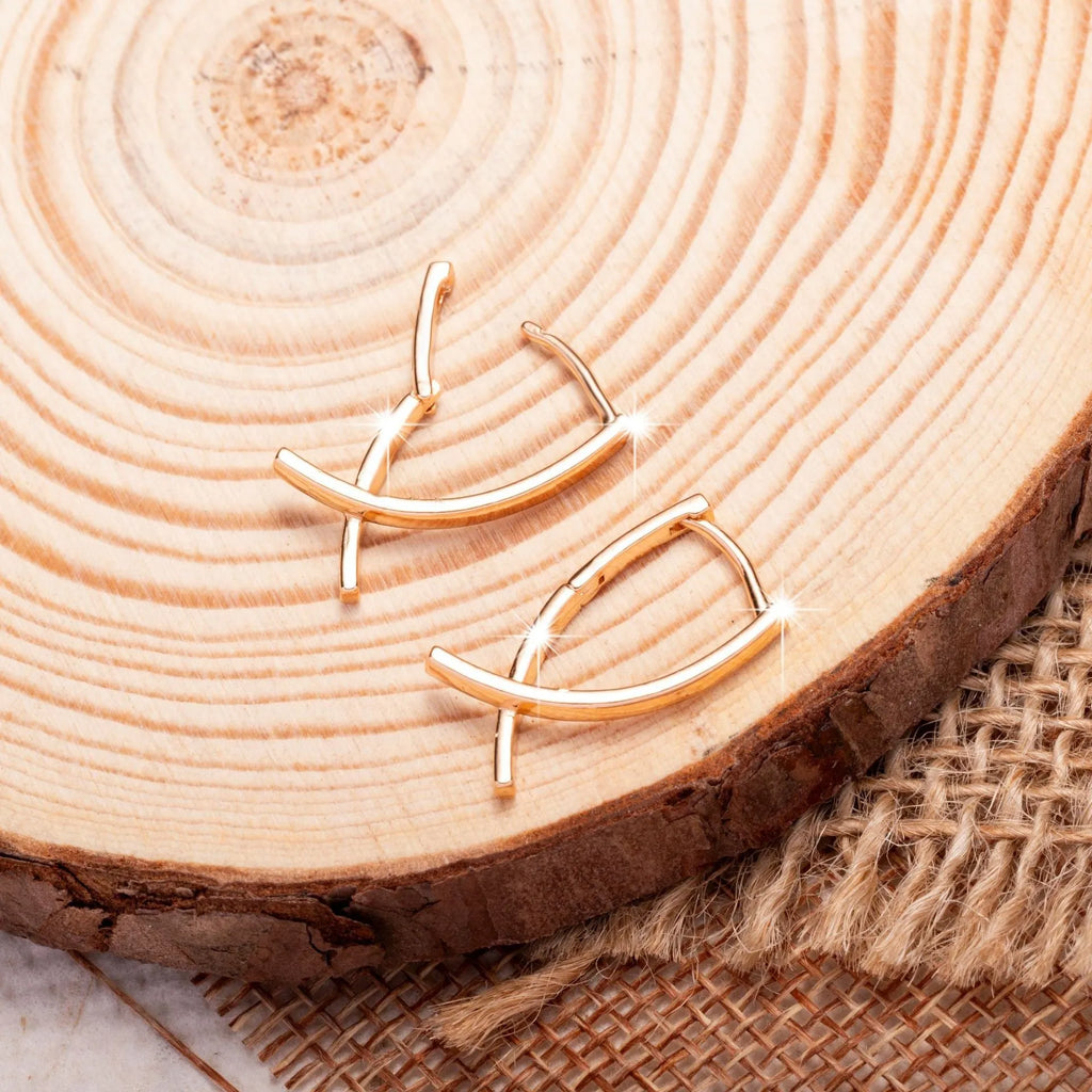 A pair of rose gold coloured cross shaped earrings made from copper on a white background.
