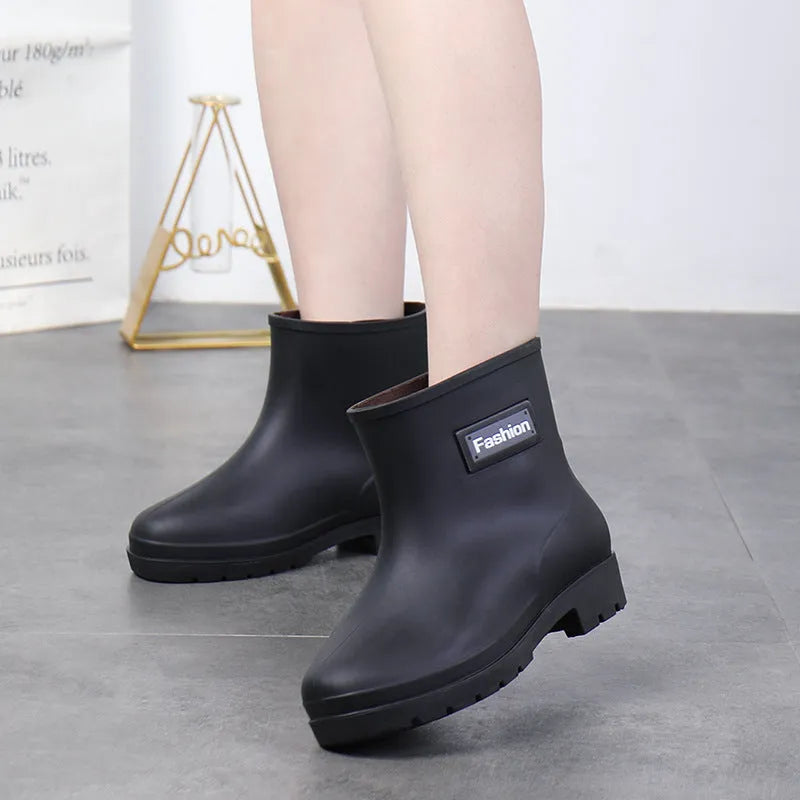 Women's black PVC mid-calf rain boot with low heel on a wet surface