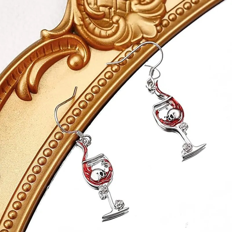 A pair of silver-toned Halloween earrings combining a skull design with a wine glass shape.