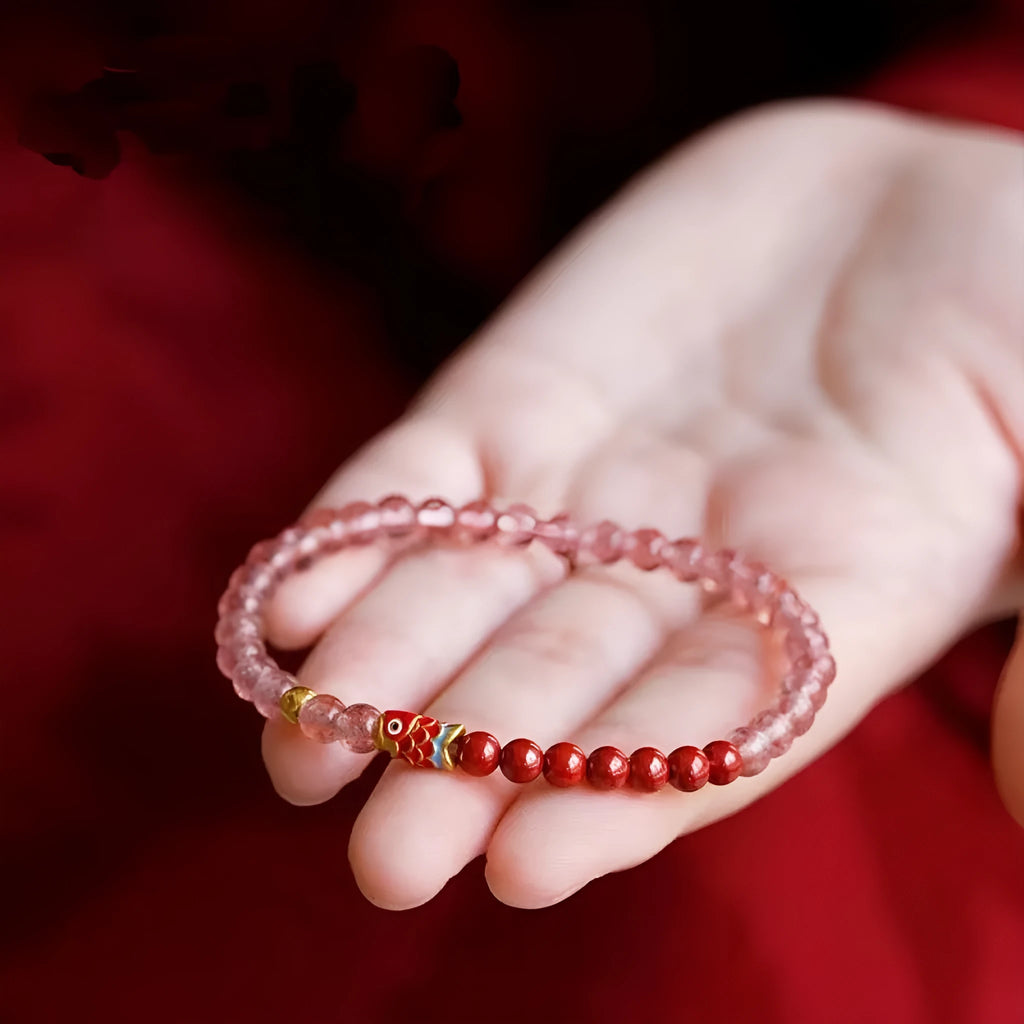 Purple cinnabar and strawberry quartz bracelet with koi and peach blossom design on a wrist.