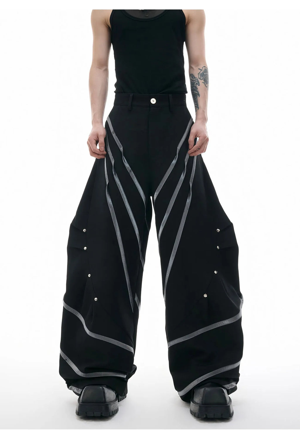 Men's black polyester trousers with metal striped rivet decoration and pleats, showing three-dimensional cut.