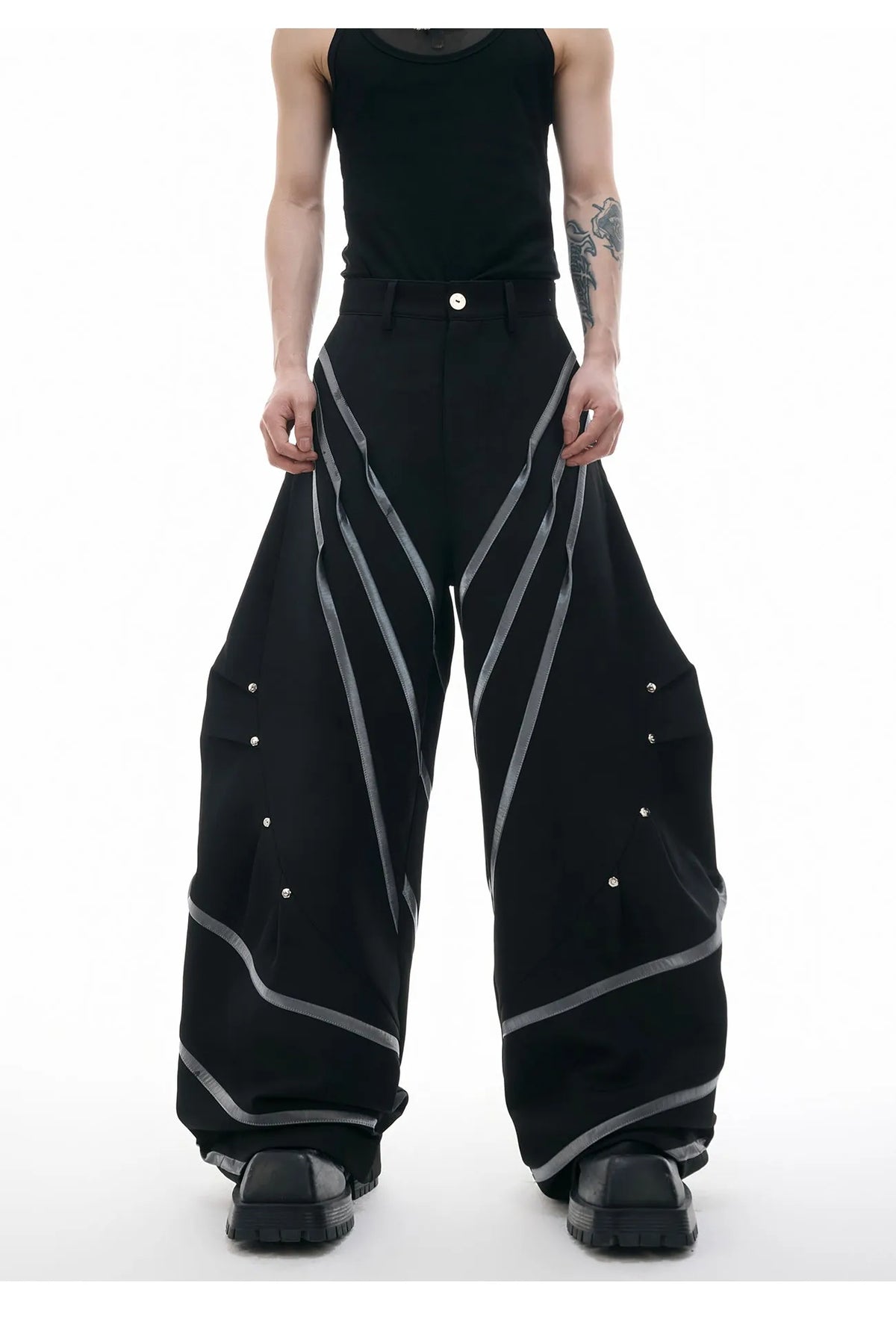 Men's black polyester trousers with metal striped rivet decoration and pleats, showing three-dimensional cut.