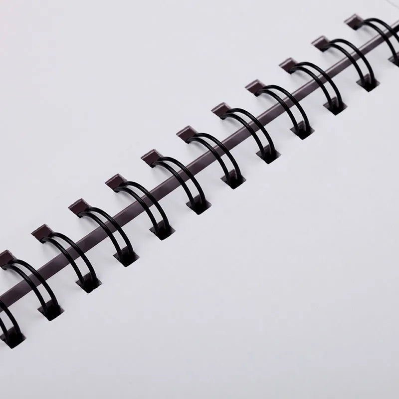 A4 sketch book with spiral coil binding lying open on a table, showing blank heavyweight paper.