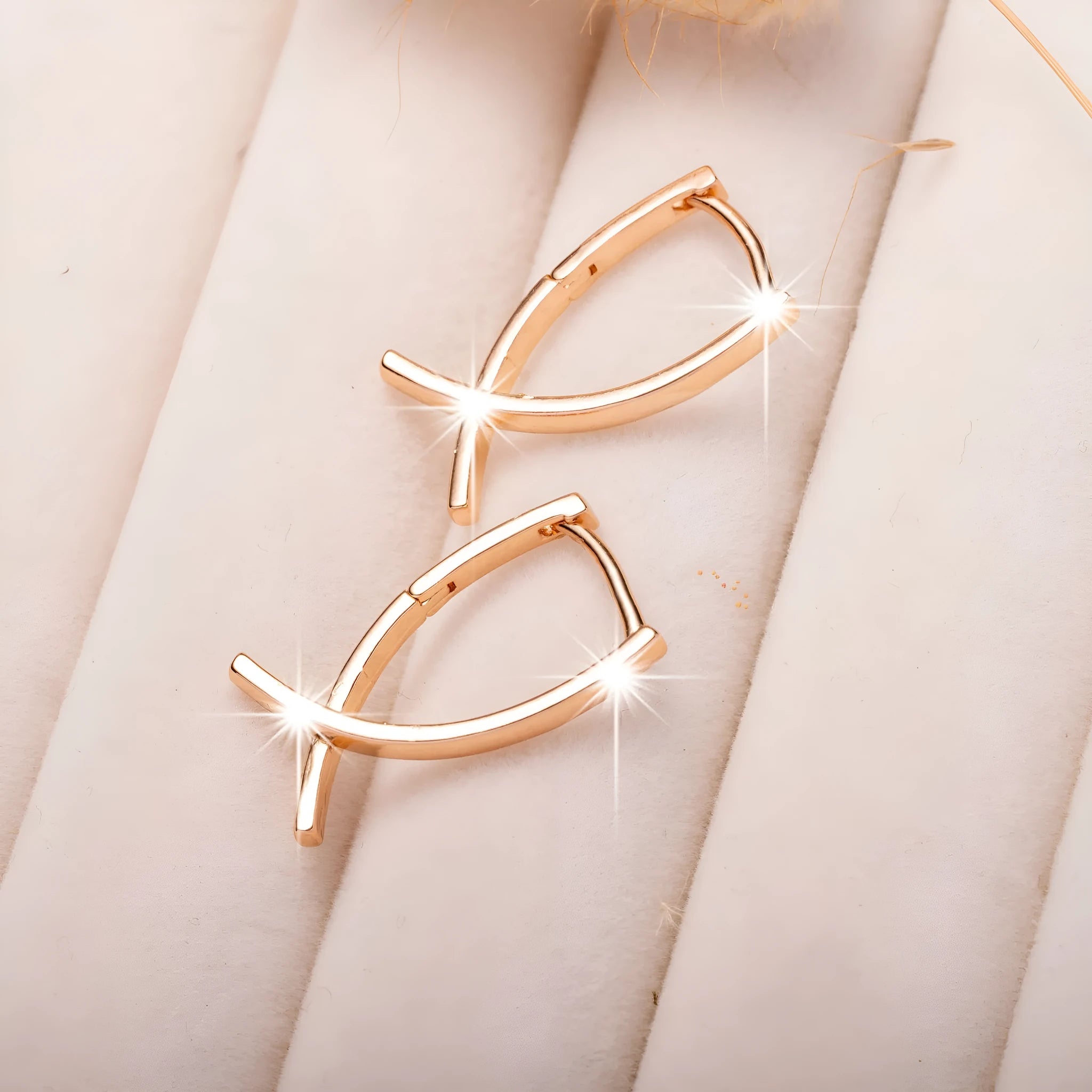 A pair of rose gold coloured cross shaped earrings made from copper on a white background.