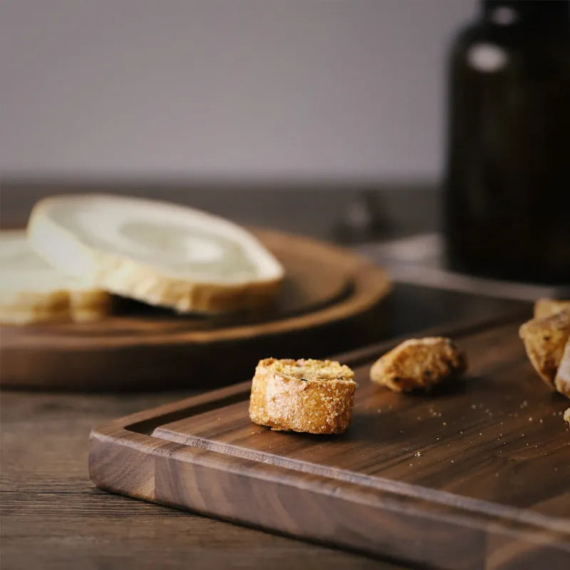 Black walnut wood chopping board with juice groove, shown in round and rectangular sizes on a kitchen counter.