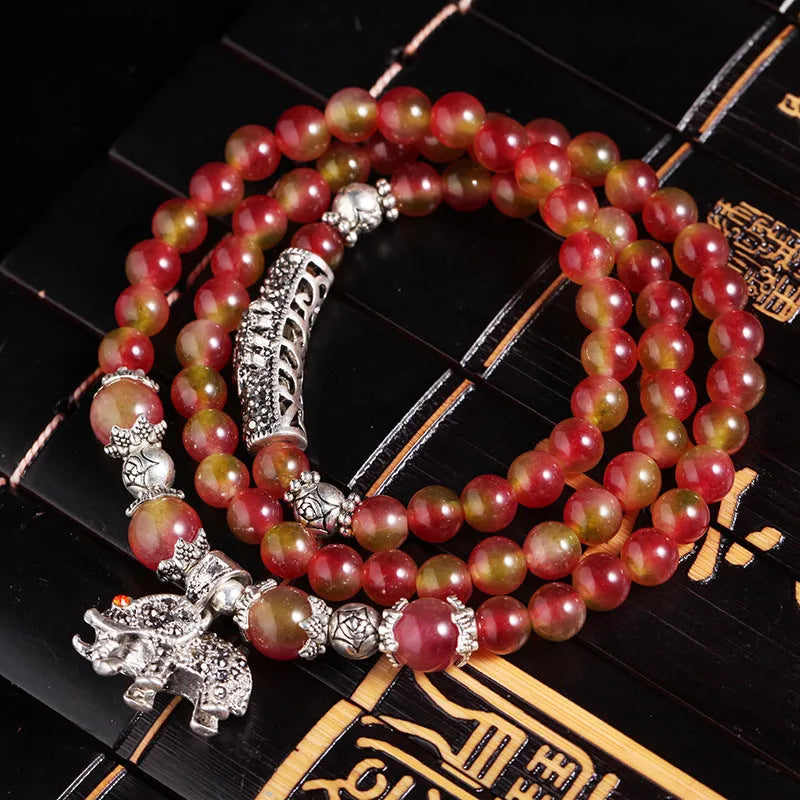 Handmade bracelet with watermelon crystal beads and a red Chinese knot on a white background.