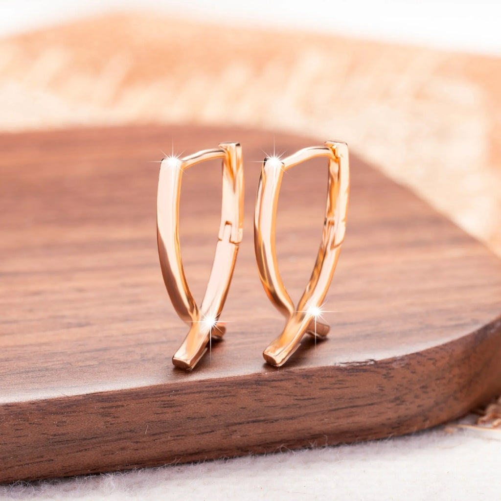 A pair of rose gold coloured cross shaped earrings made from copper on a white background.