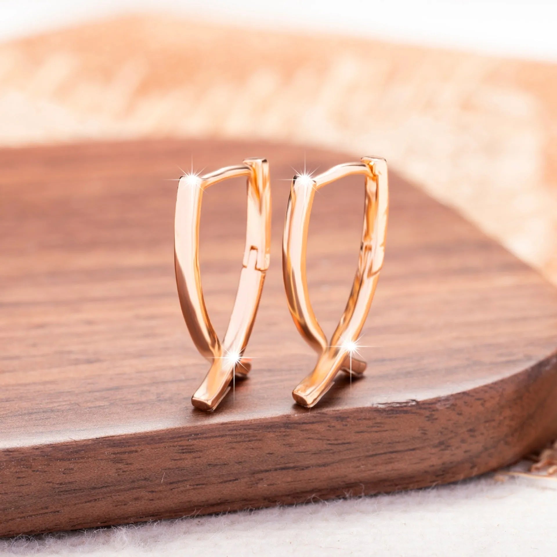 A pair of rose gold coloured cross shaped earrings made from copper on a white background.