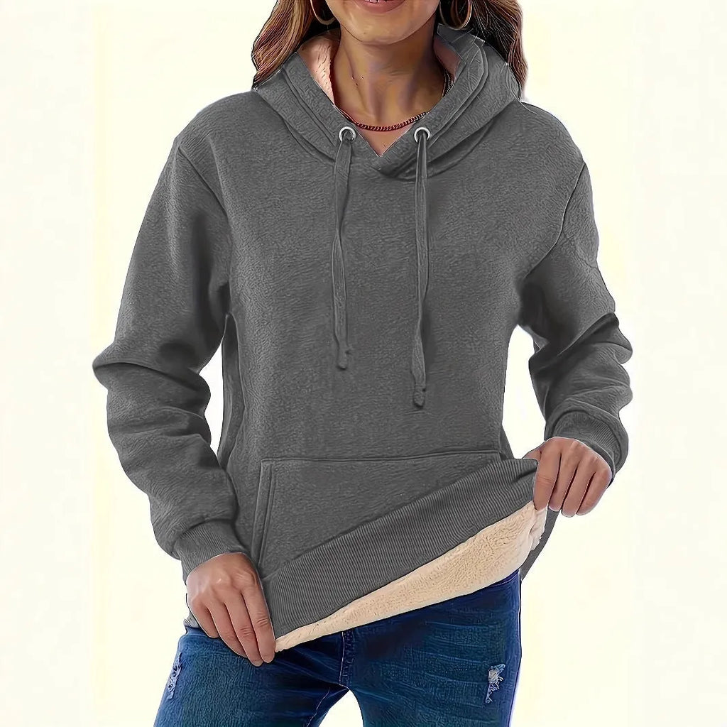 Woman wearing a thick, grey hooded sweater with a raised 3D pattern, featuring long sleeves and pockets.