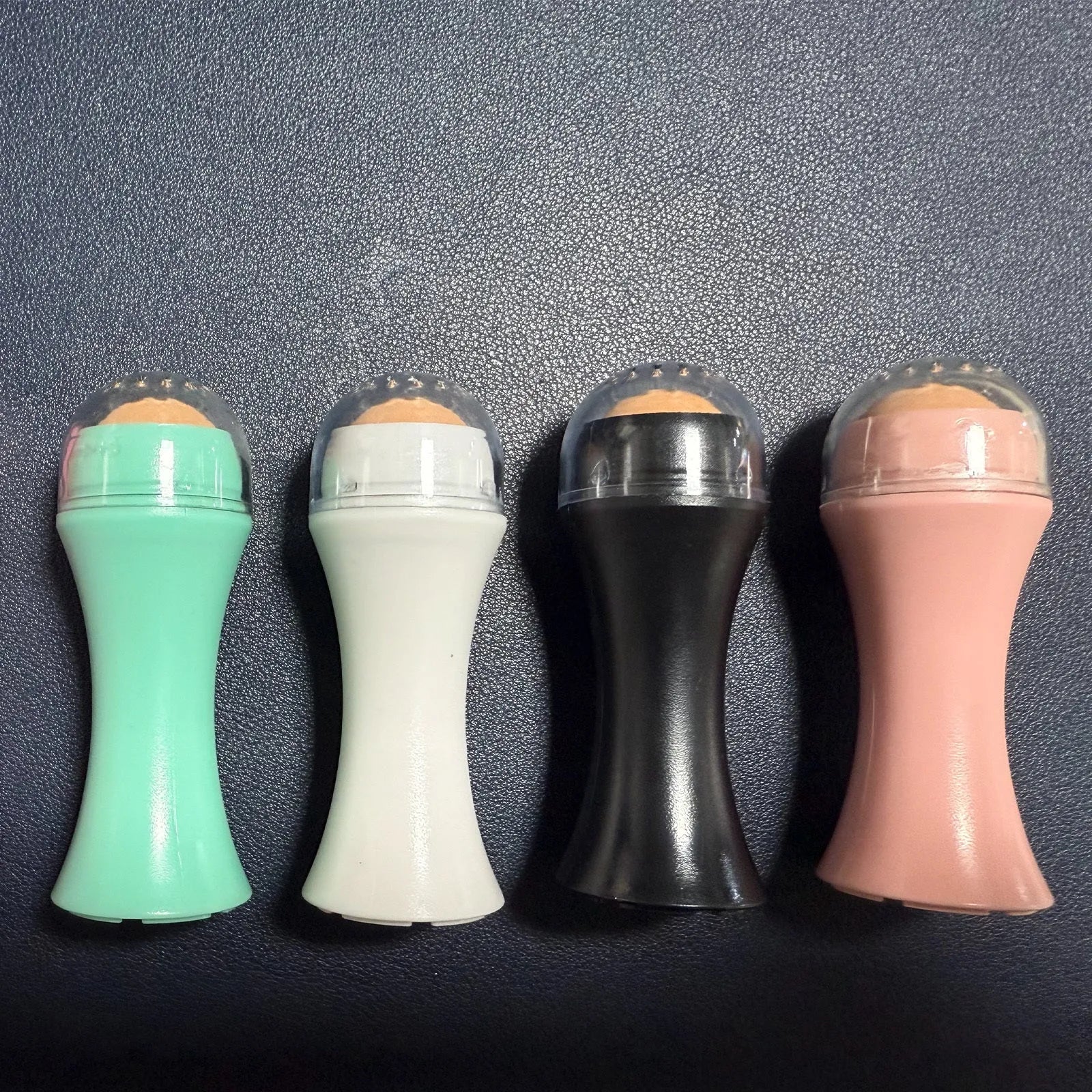 Portable volcanic stone oil-absorbing facial roller in black, green, pink, or white on a plain background.