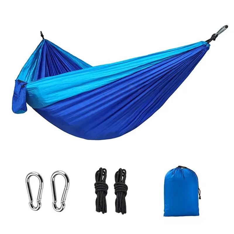 Blue nylon parachute cloth camping hammock hung between two trees outdoors.