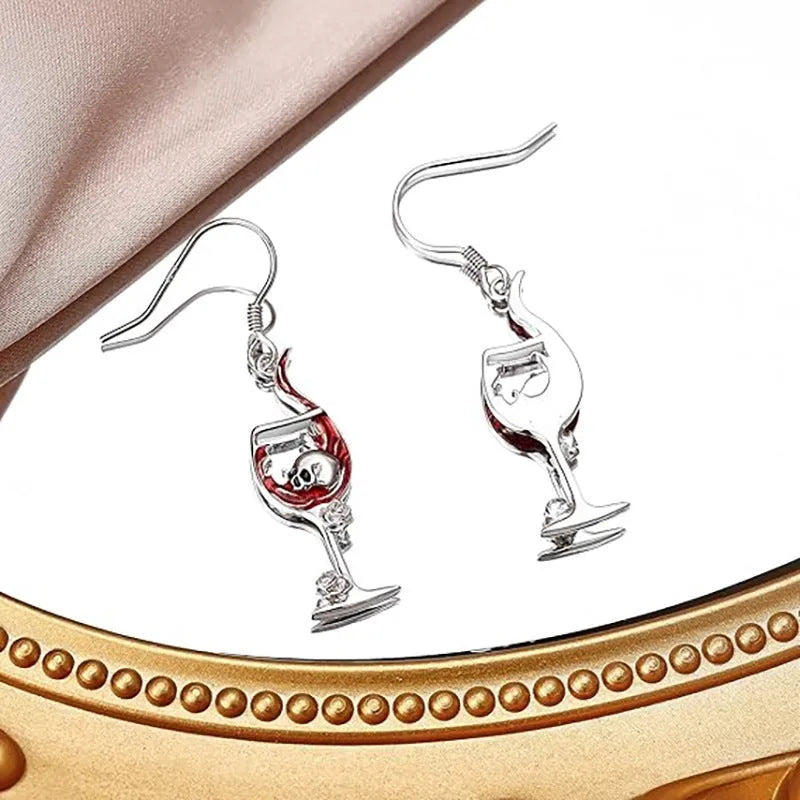 A pair of silver-toned Halloween earrings combining a skull design with a wine glass shape.
