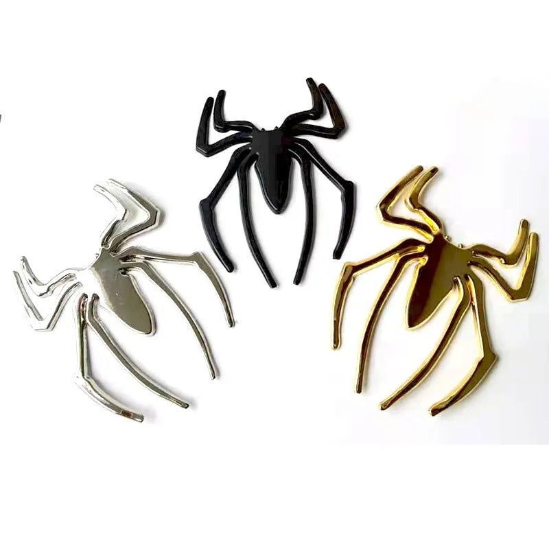 Three-dimensional zinc alloy spider bumper sticker in metallic colours on a surface.