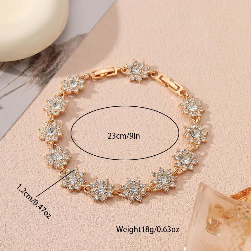 Gold tone flower-shaped bracelet with blue crystal gems on a wrist.