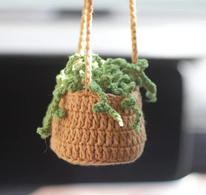 Green and white knitted car plant decoration with hanging rope on car dashboard