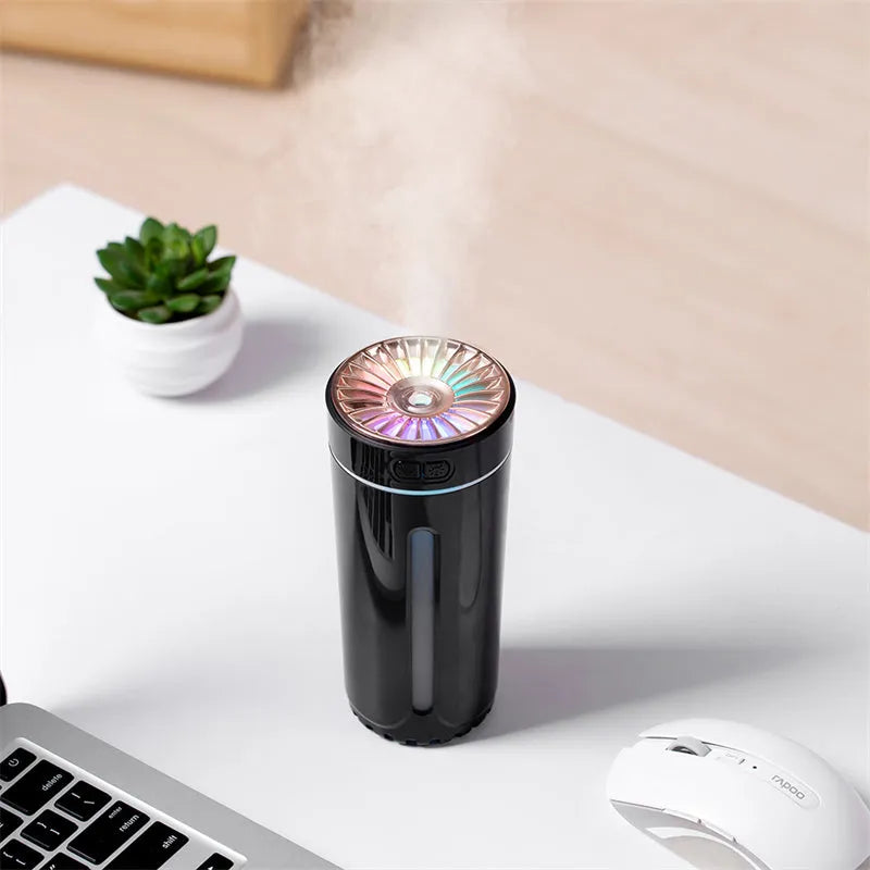 Black portable USB rechargeable car humidifier with colourful lights on a desk next to a cup