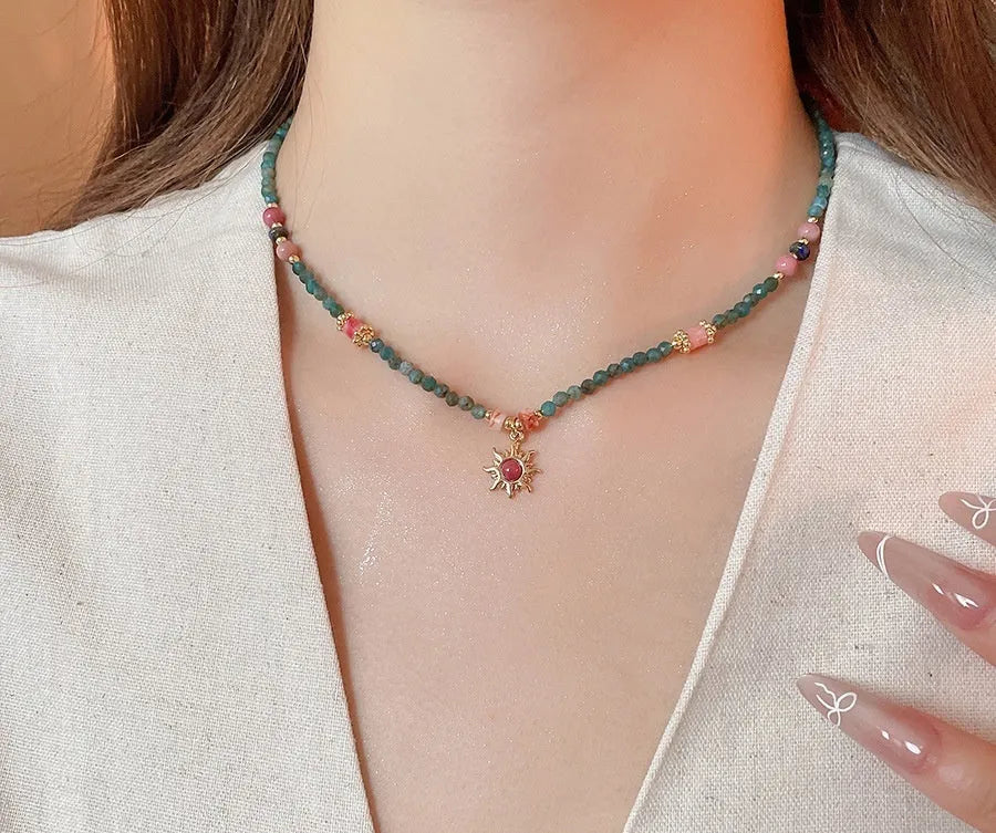 Freshwater pearl necklace with a geometric stone sun pendant on a gold, blue, and pink chain.