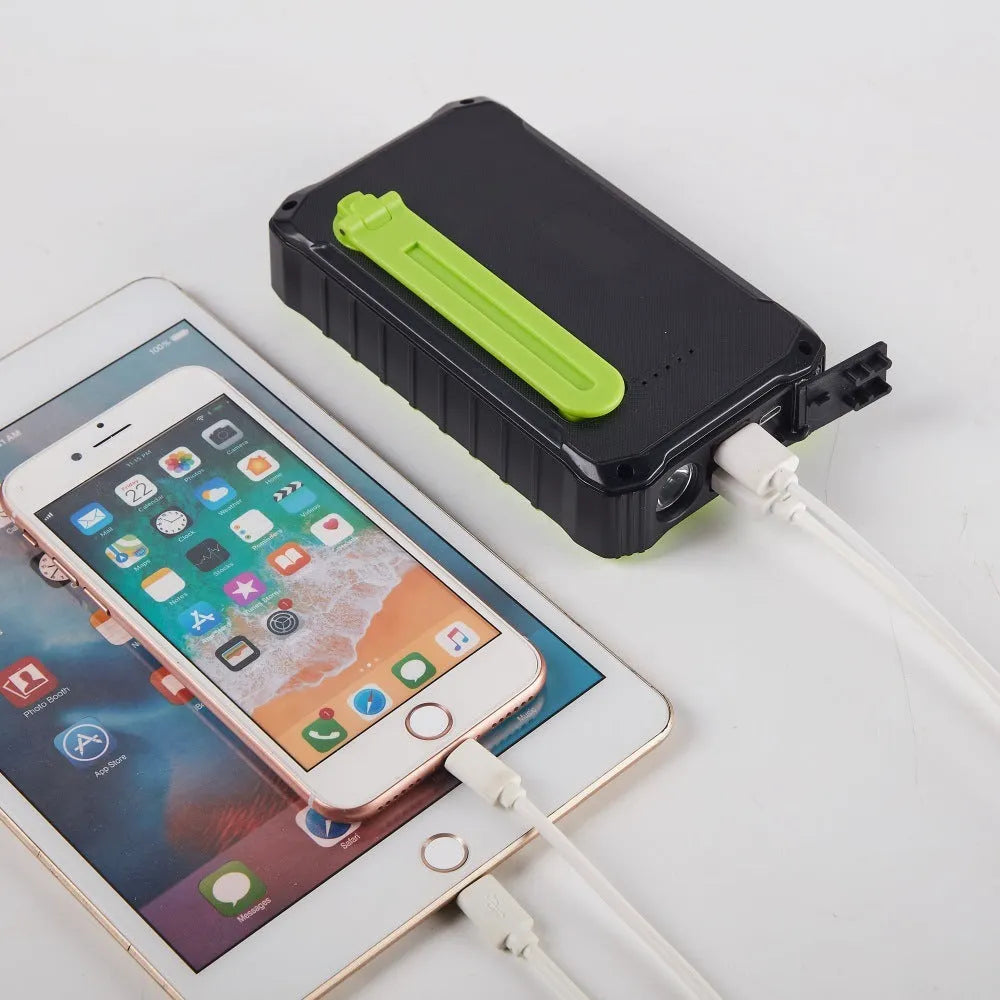 Orange and green hand-crank solar power bank with LED torch and dual USB ports showing 12000mAh capacity