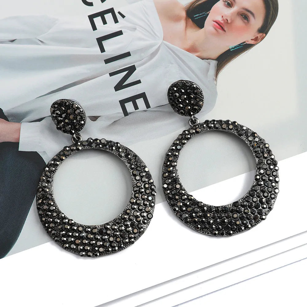 A pair of large round metal pendant earrings with diamond detailing in a cartoon style.